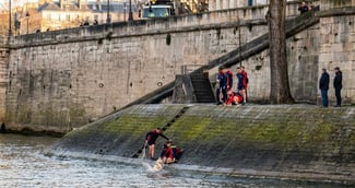 Des pompiers de Paris secourant un petit chien mouillé sur les quais de la Seine sous le regard soulagé de sa maîtresse.