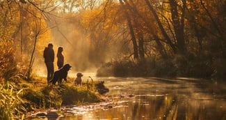 Deux femmes et un grand chien noir près d'un ruisseau découvrent un Caniche blanc égaré, symbolisant espoir et sauvetage.